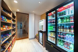 Zona de snacks y bebidas con estantes llenos de diversas opciones y un refrigerador con bebidas.