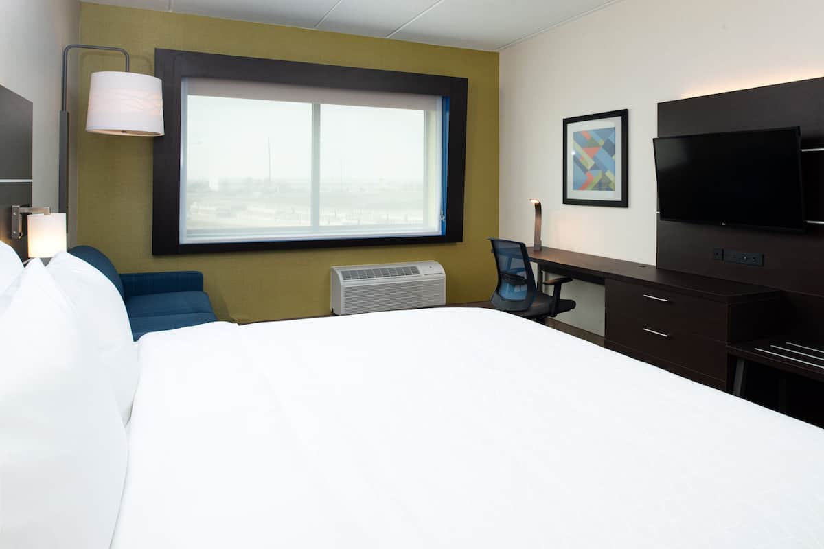 A hotel room with a large bed, a desk with a chair, a television, and a window with a view.