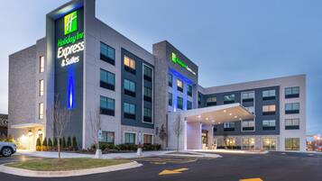 A Holiday Inn Express & Suites hotel with a modern design, featuring a prominent sign, a covered entrance, and a parking lot with directional arrows.