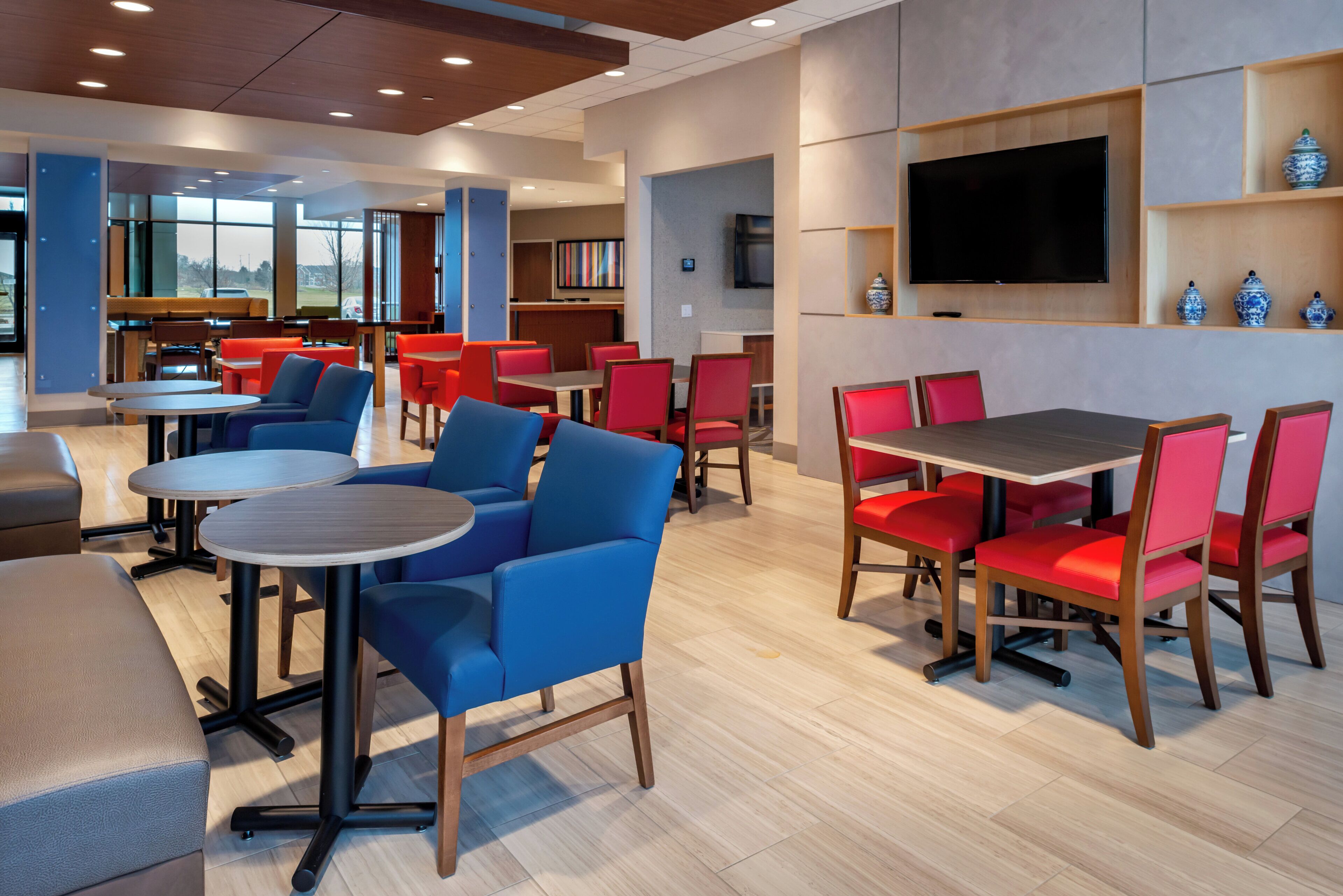 A modern hotel lobby with seating areas, a flat-screen TV, and a view of the outdoors.