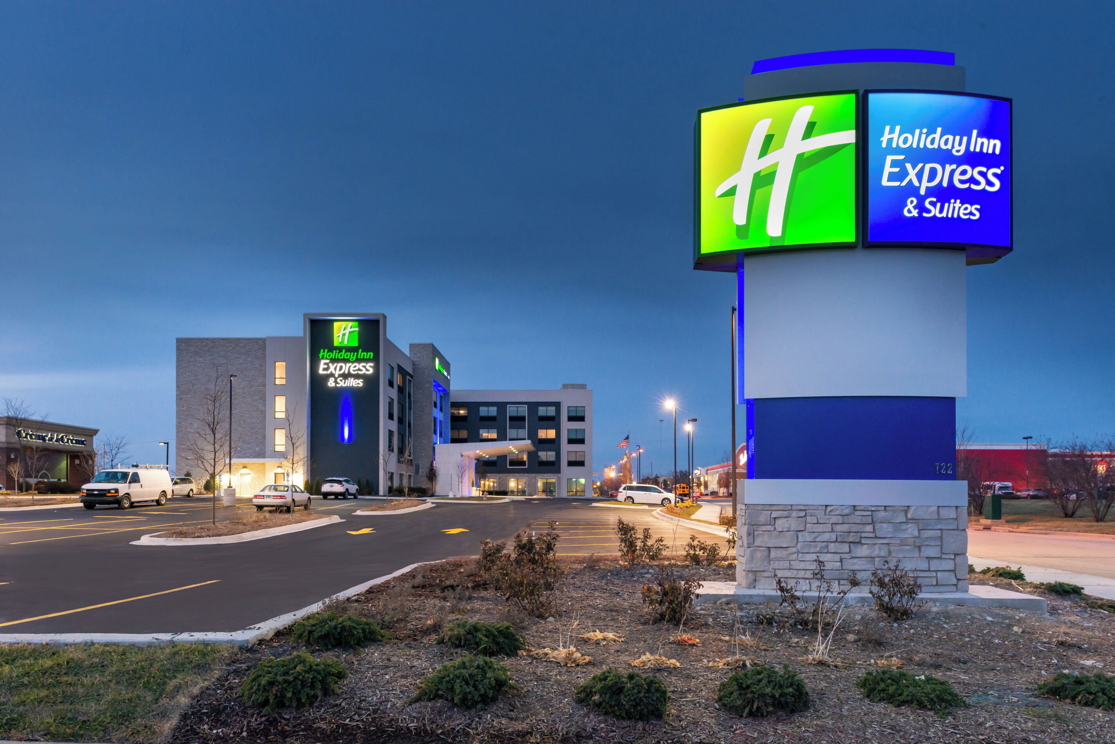 A Holiday Inn Express & Suites hotel with a prominent sign, a parking lot, and a building with a brick facade.