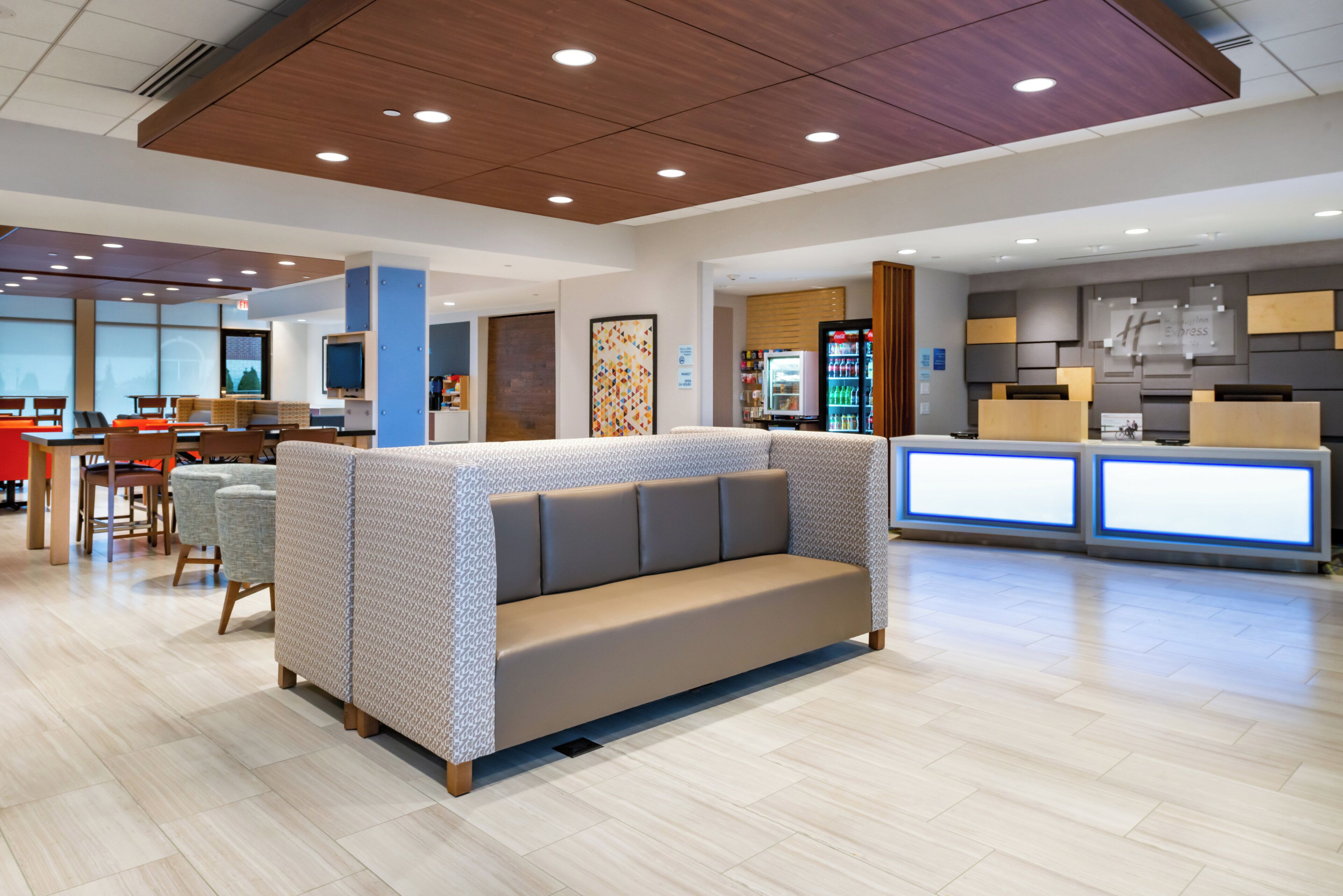 A modern hotel lobby with a seating area, a reception desk, and a vending machine.