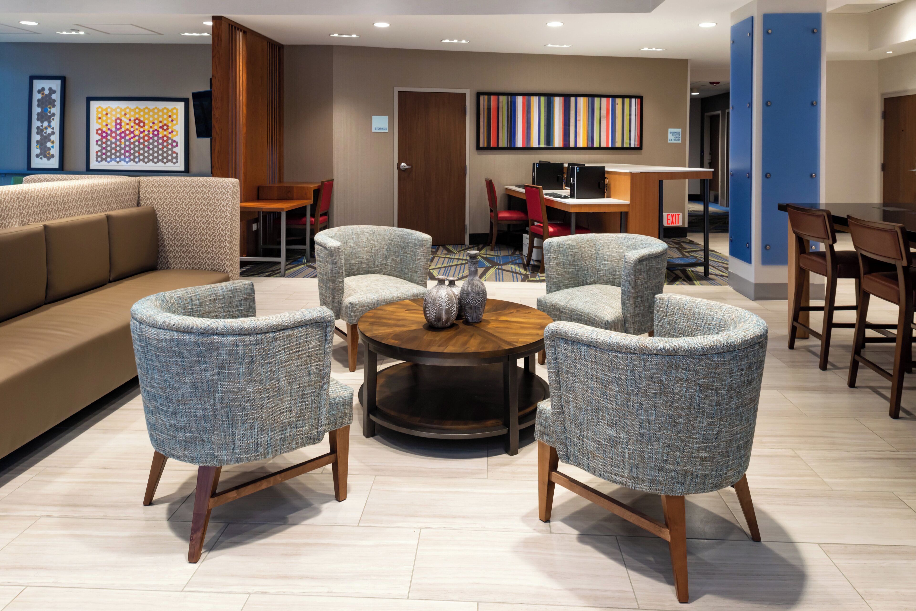 A modern lounge area with a sofa, armchairs, a coffee table, and a desk with computers.