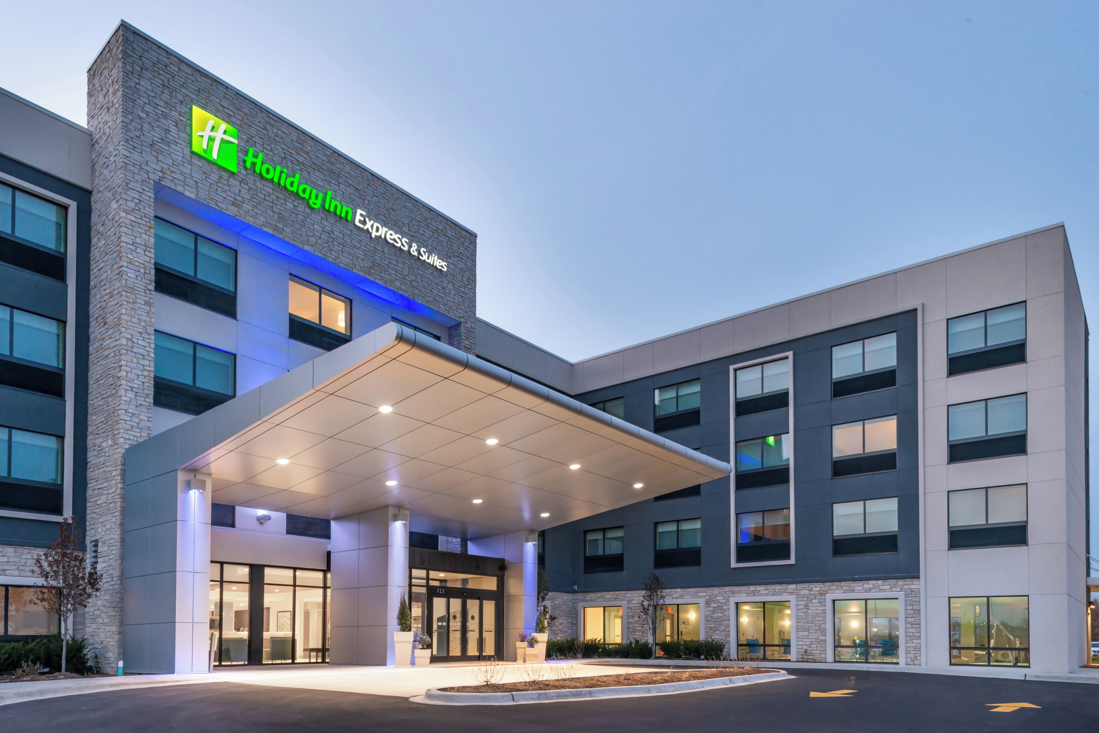Un moderno edificio de hotel con un llamativo letrero de 'Holiday Inn Express & Suites', una entrada cubierta y una fachada bien iluminada.