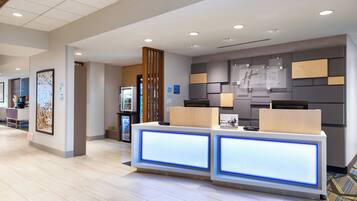 Un espace d’accueil d’hôtel au design moderne, comprenant un comptoir d’accueil doté de panneaux rétroéclairés, une enseigne murale pour Holiday Inn Express et un réfrigérateur en arrière-plan.