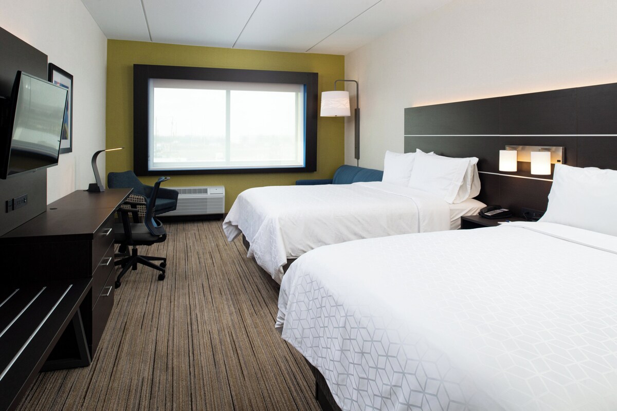 Een hotelkamer met twee bedden, een bureau, een stoel, een televisie en een raam.