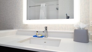 A bathroom with a white sink, a mirror, a towel rack, and a tissue dispenser. - Holiday Inn Express & Suites Romeoville - Joliet North by IHG (Romeoville)
