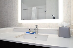 Een badkamer met een witte wastafel, een spiegel, een handdoekhouder en een tissuespender.