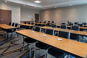 A conference room with multiple tables and chairs, carpeted flooring, and a plain wall with a door and a light switch. - Holiday Inn Express & Suites Romeoville - Joliet North by IHG (Romeoville)