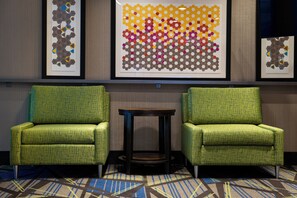Une chambre d’hôtel avec deux fauteuils verts, une petite table ronde et trois œuvres d’art abstraites encadrées accrochées au mur.