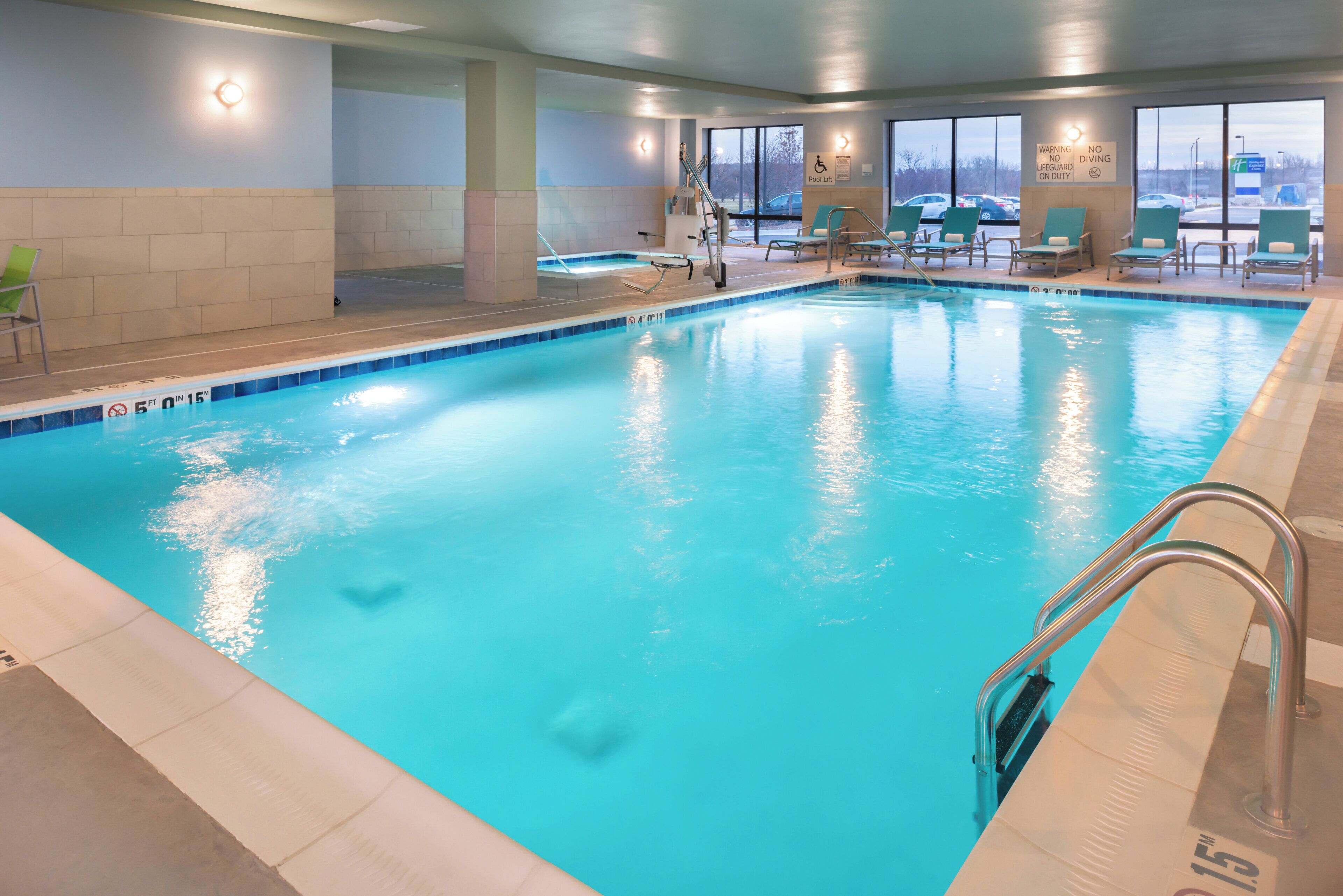 An indoor swimming pool with clear water, a pool lift, and lounge chairs.