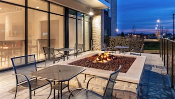 An outdoor seating area with tables and chairs, a fire feature, and a stone wall.