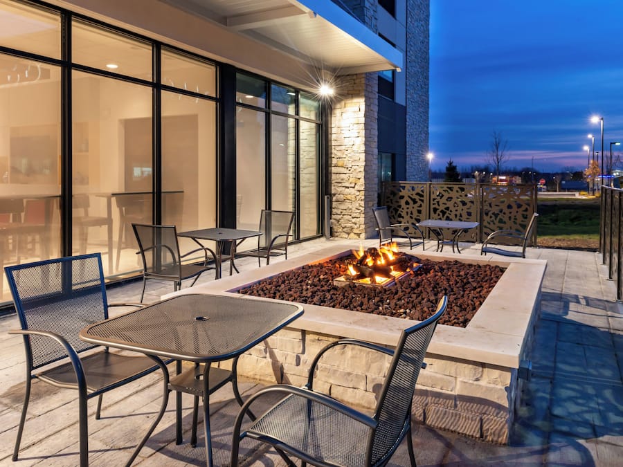 An outdoor seating area with tables and chairs, a fire feature, and a stone wall.
