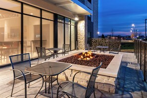 An outdoor seating area with tables and chairs, a fire feature, and a stone wall. - Holiday Inn Express & Suites Romeoville - Joliet North by IHG (Romeoville)