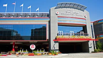 A modern building with a large glass facade, a prominent entrance with a rose emblem, and multiple flags on the roof.