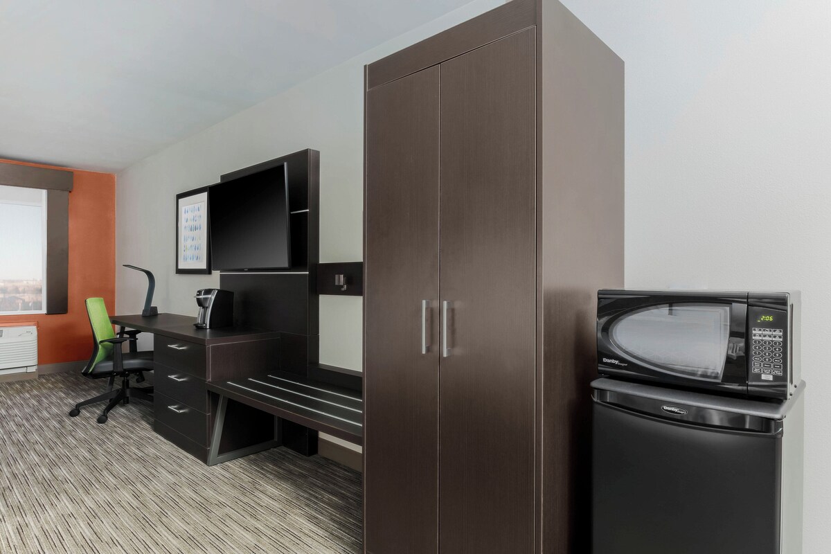 A hotel room with a desk, chair, wardrobe, and a microwave.