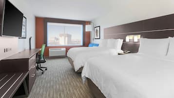 A hotel room with two beds, a desk, a chair, a large window with a city view, and a flat-screen TV mounted on the wall.