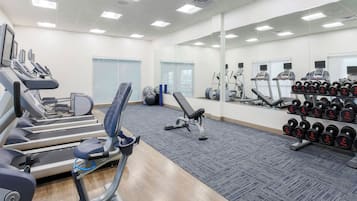 A gym with treadmills, elliptical machines, and a rack of dumbbells.