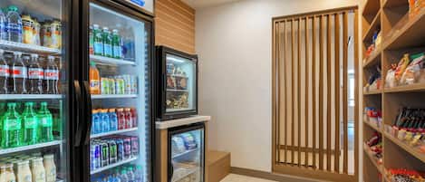 A beverage refrigerator stocked with various drinks, a smaller fridge below it, and shelves with snacks and condiments.