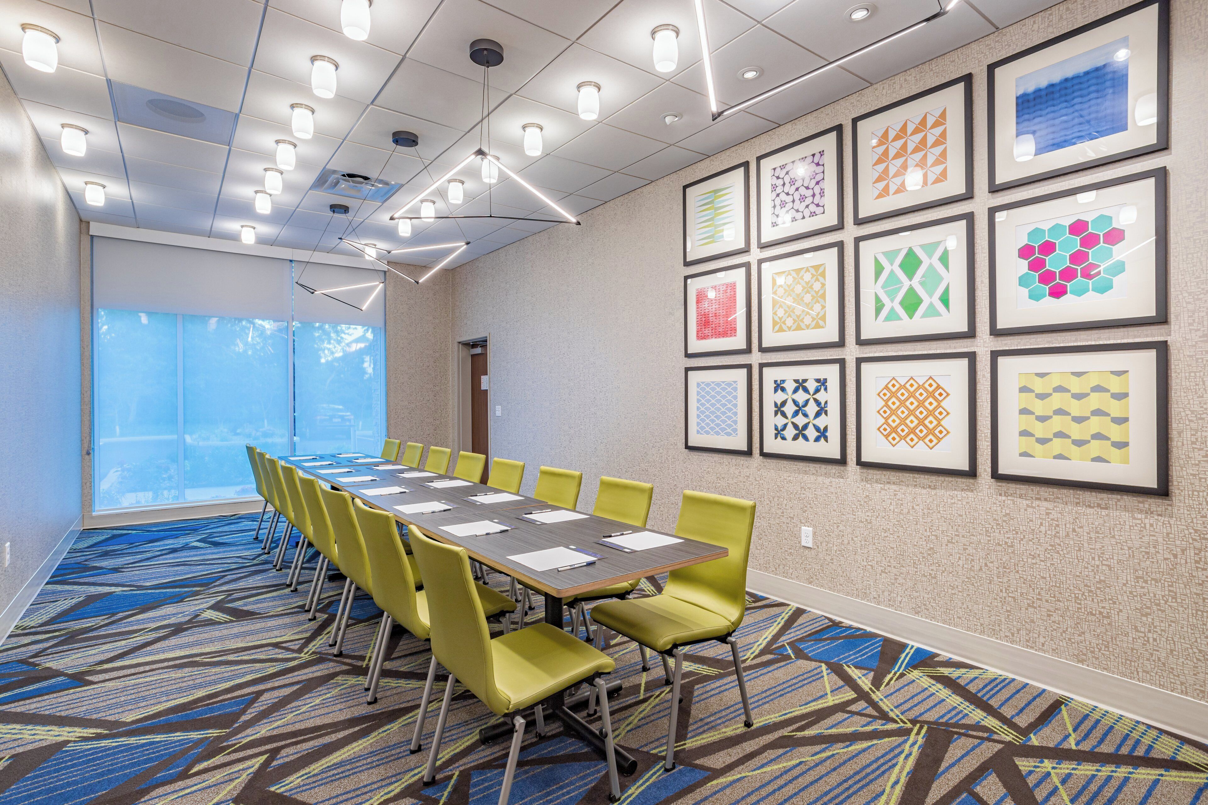 A conference room with a long table, yellow chairs, and framed artwork on the walls.