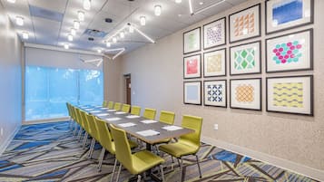 A conference room with a long table, yellow chairs, and framed artwork on the walls.