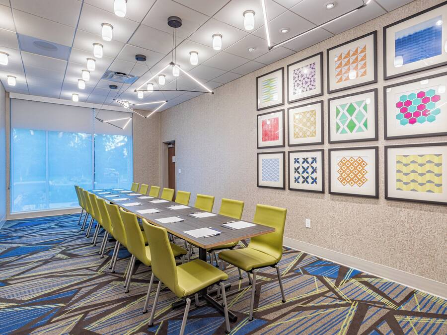 A conference room with a long table, yellow chairs, and framed artwork on the walls.