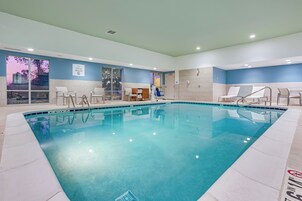 Ein Hallenbad mit klarem Wasser, umgeben von weiß gefliesten Wänden und einer blauen Akzentwand. Mehrere Liegestühle und ein Umkleideraum sind zu sehen.