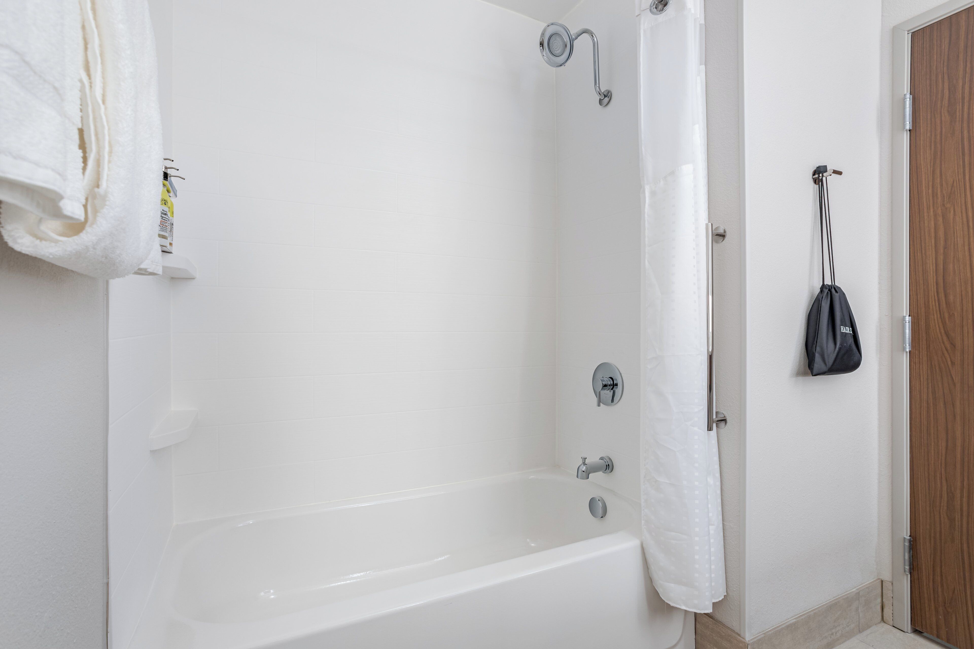 Une salle de bain avec une baignoire blanche, une serviette accrochée au mur et une porte en bois.