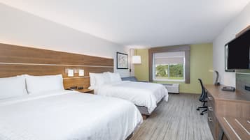 A hotel room with two beds, a desk, a chair, a TV, and a window with a view of greenery.
