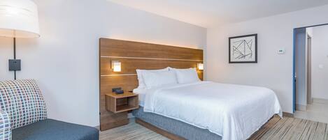 A hotel room with a bed, bedside table, lamp, and a framed abstract artwork on the wall.