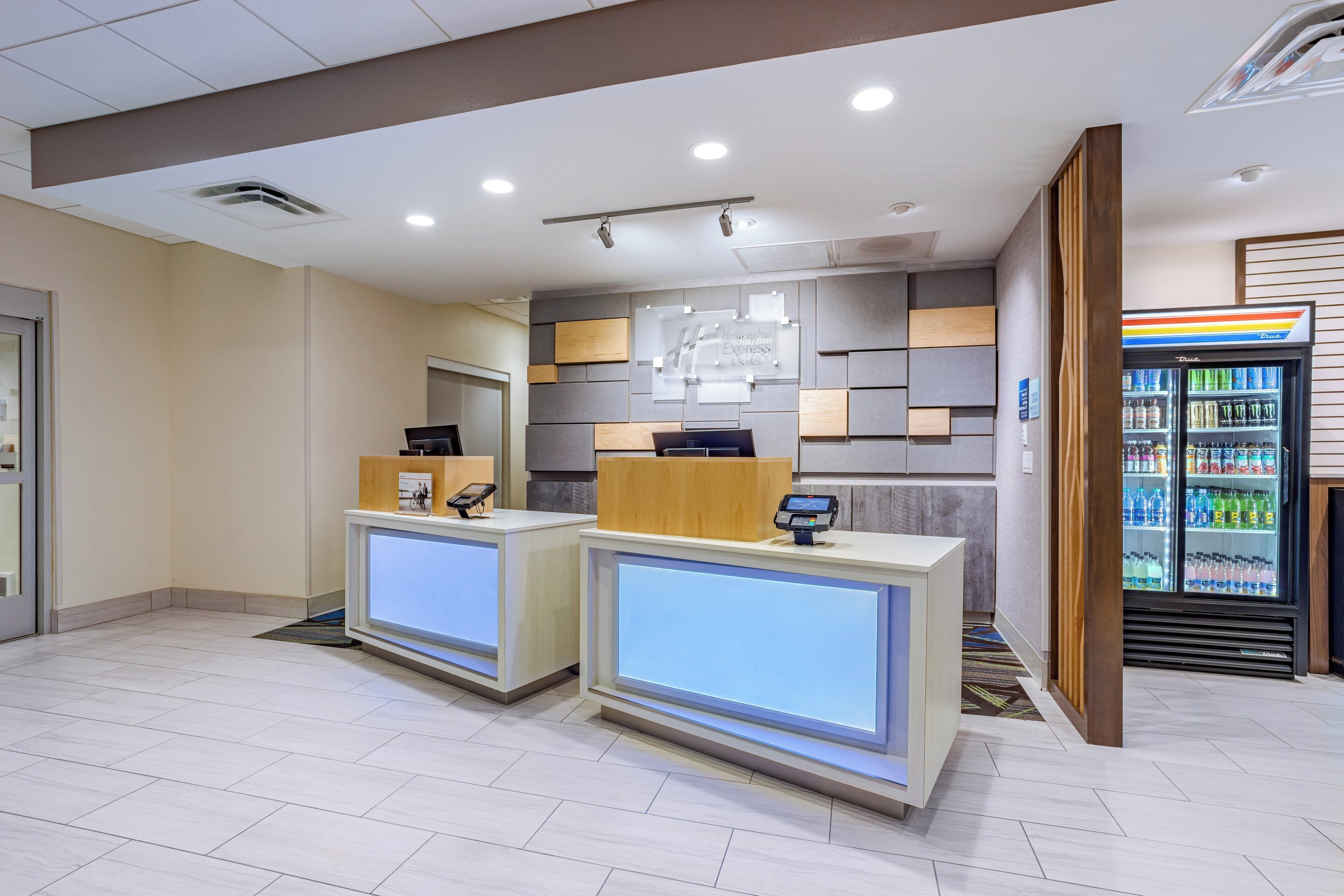 A hotel reception area with two reception desks, a wall-mounted information board, and a beverage dispenser.