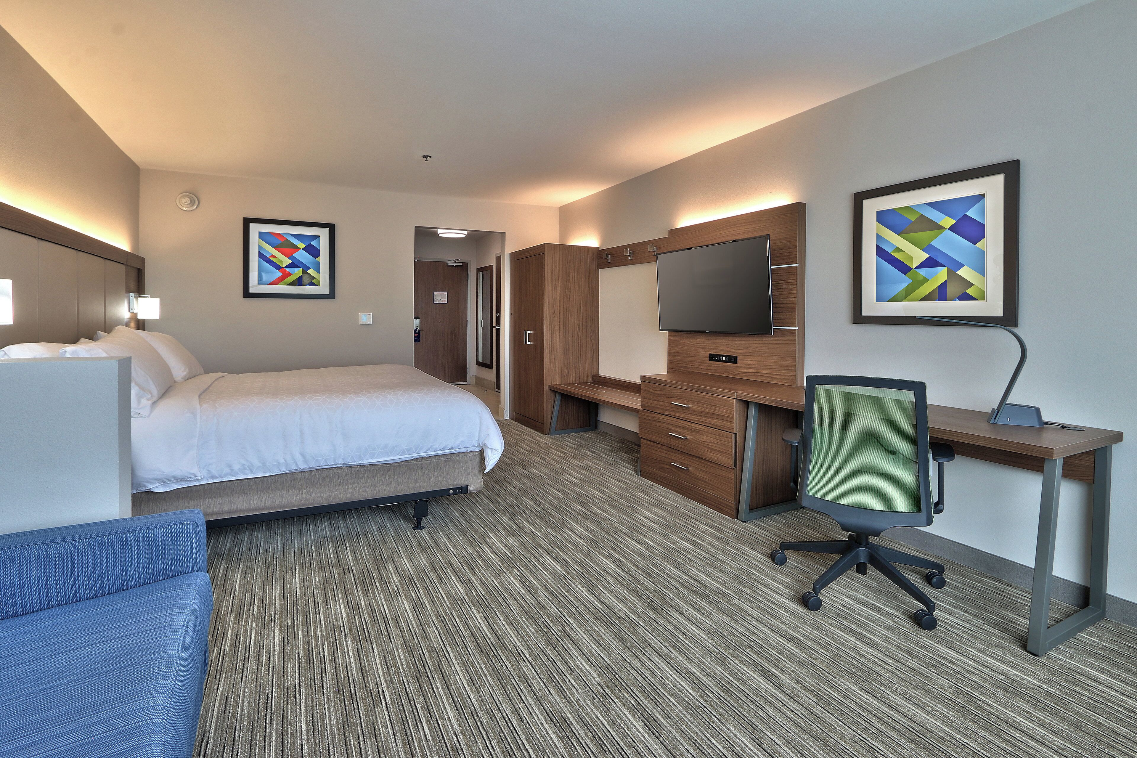 A hotel room with a bed, desk, chair, and artwork on the walls.