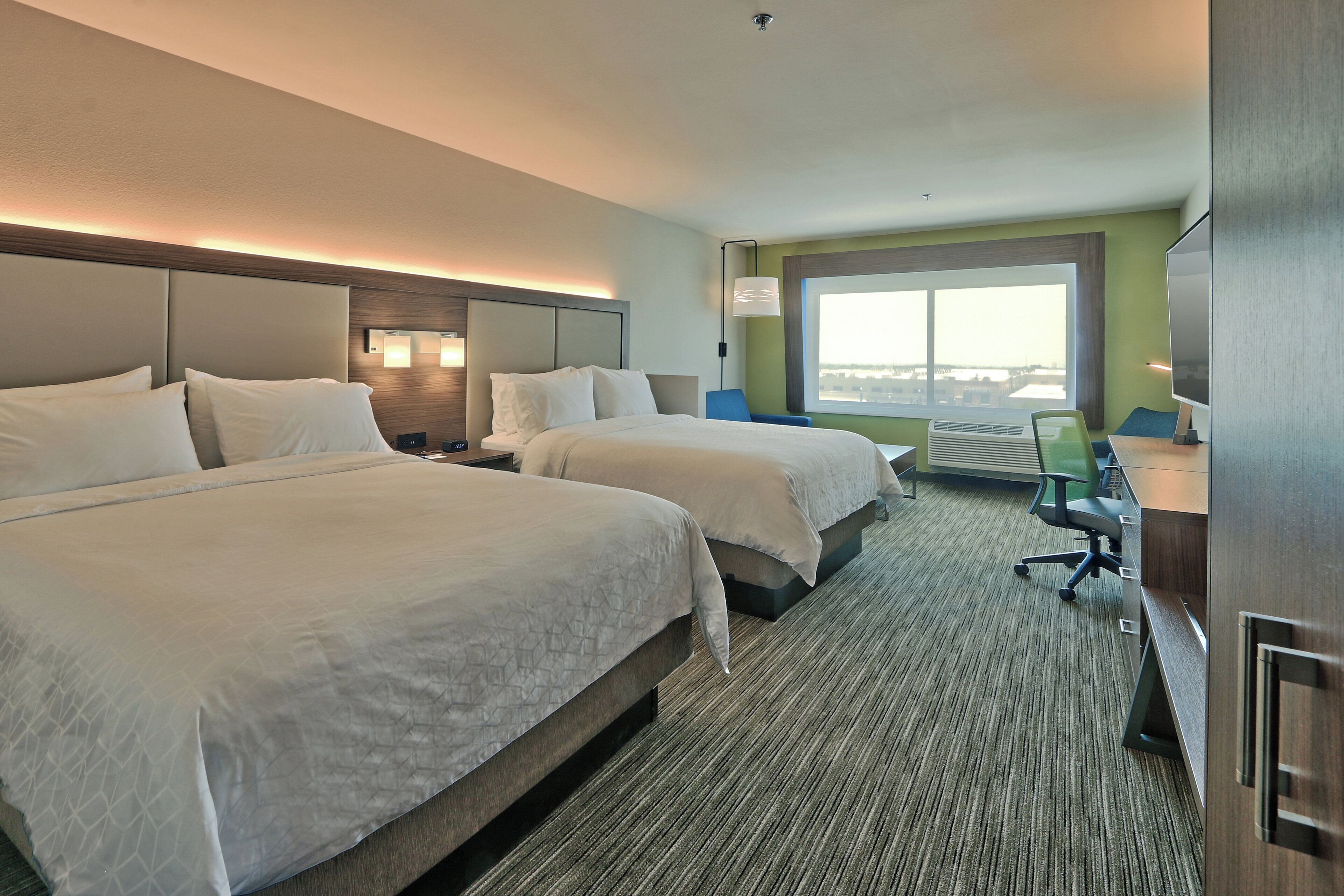 A hotel room with two beds, a desk, a chair, and a large window.
