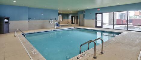 An indoor swimming pool with a lifeguard chair, a pool ladder, and a clear exit sign.