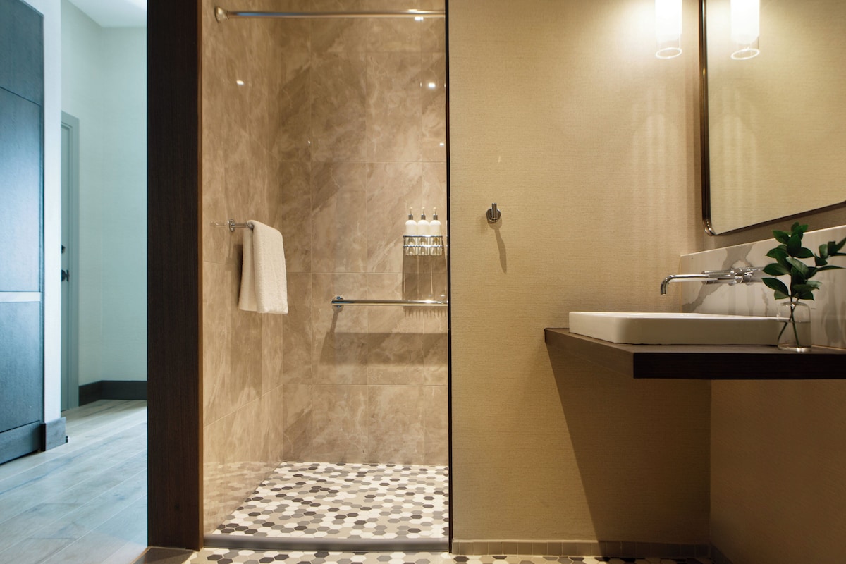 Un baño moderno con cabina de ducha de vidrio, un lavabo con espejo y una planta pequeña en la encimera.