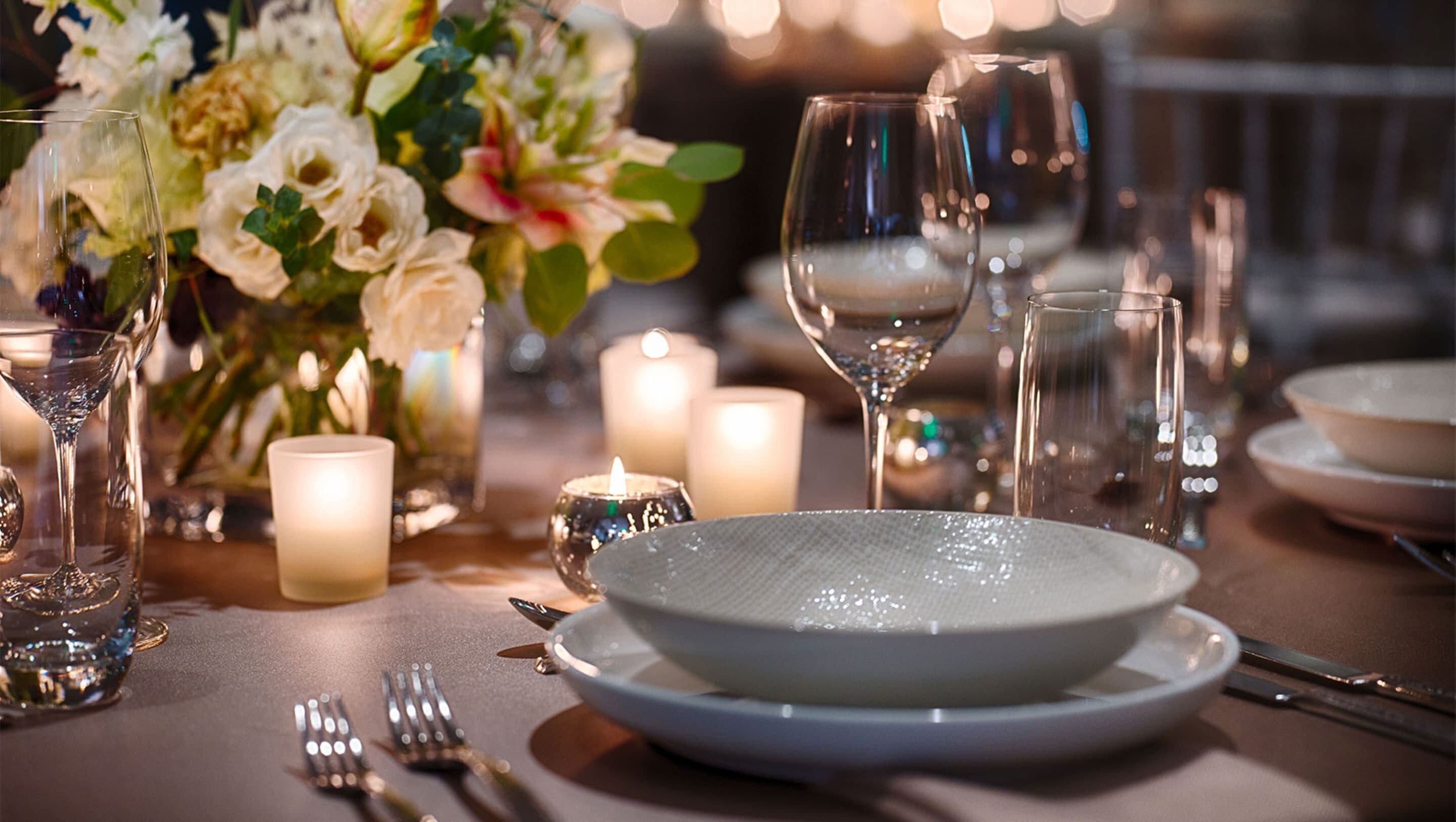 Una mesa dispuesta para una comida, con un bol, copas de vino y velas.