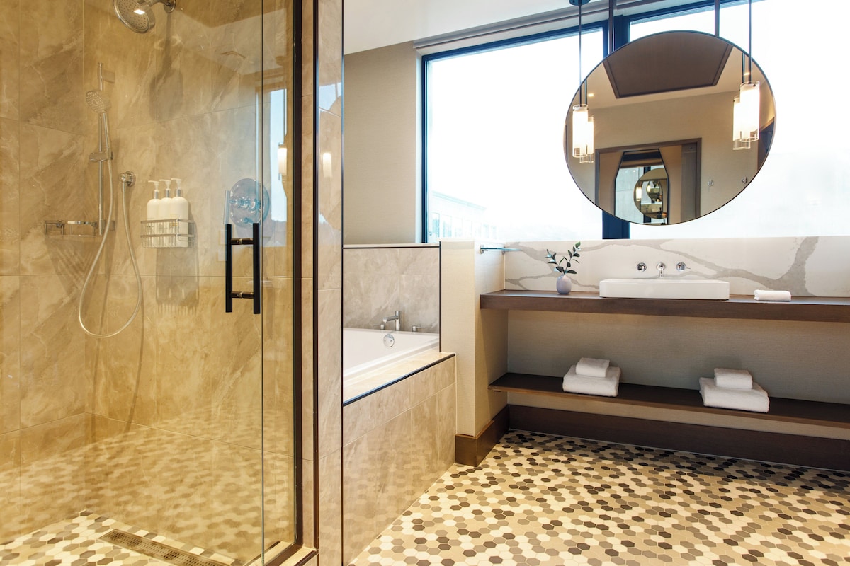 Un baño moderno con ducha de vidrio, un espejo grande y suelo de mármol.