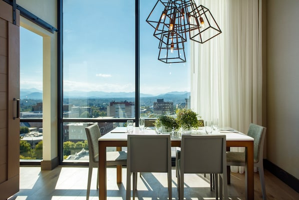 Comedor con un gran ventanal que ofrece vista a la ciudad, una mesa de madera y sillas.
