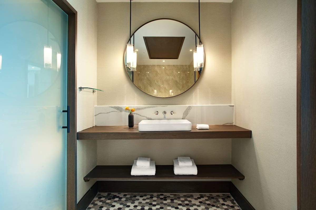A modern bathroom with a round mirror, white sink, and two towel racks.