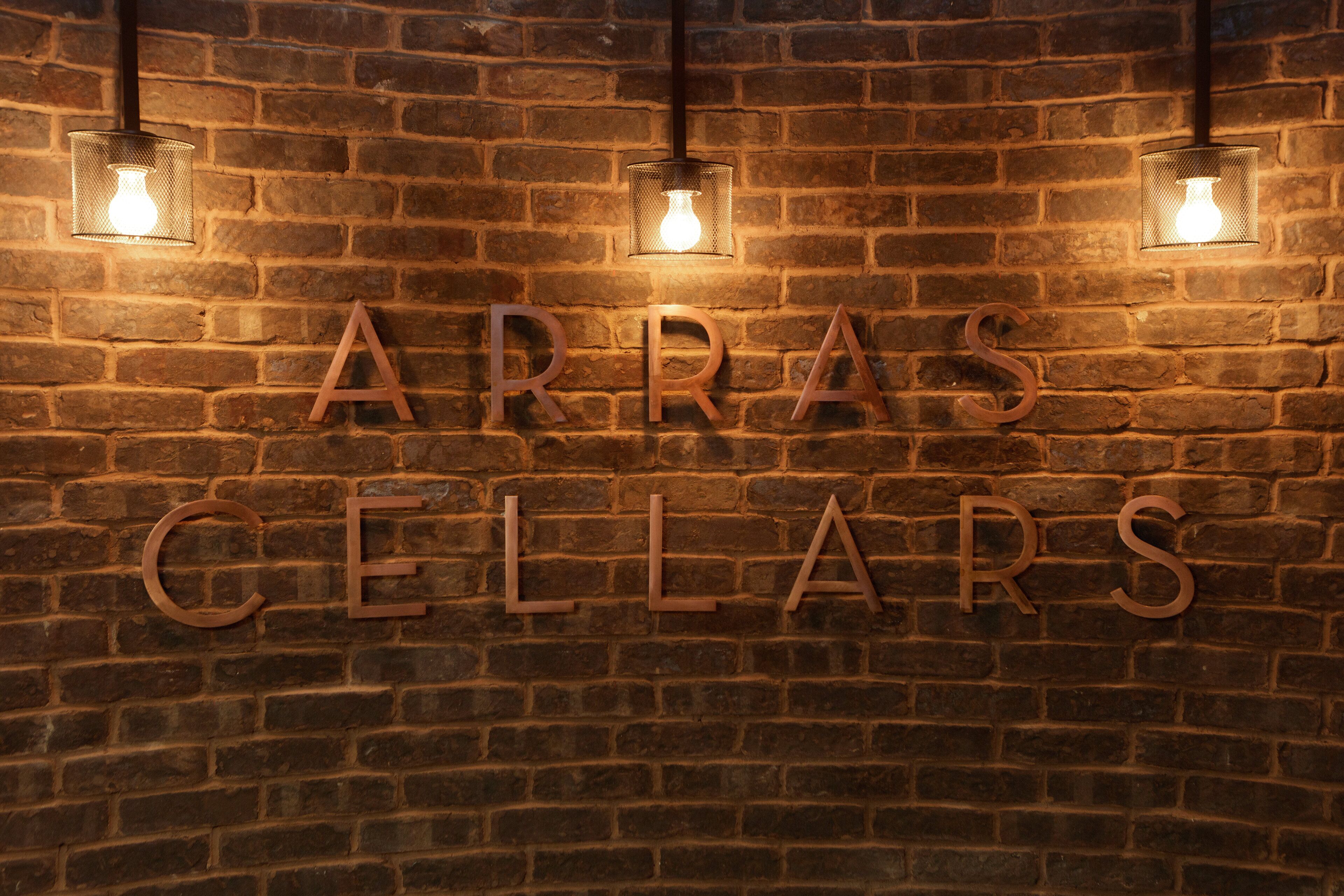 Un muro de ladrillo con las palabras "ARRAS CELLARS" iluminadas por luces colgantes.