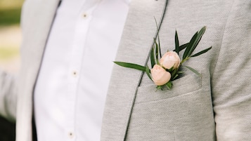 A person wearing a light grey suit with a boutonniere of a peach flower and green leaves pinned to the lapel.