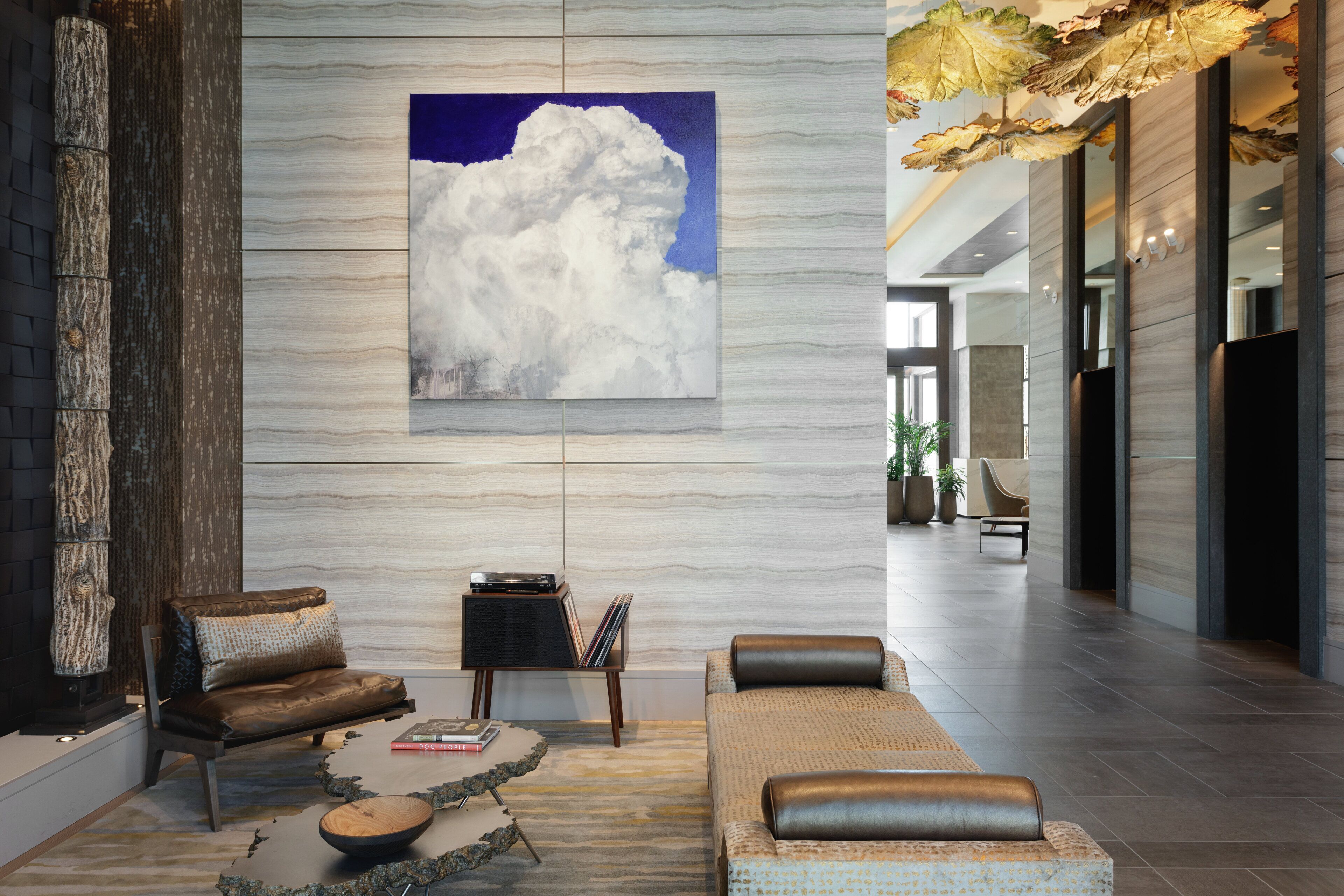 A modern lobby with a large cloud painting, leather sofas, a coffee table, and a stone sculpture.