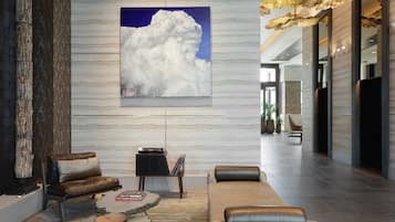 A modern lobby with a large cloud painting, leather sofas, a coffee table, and a stone sculpture.