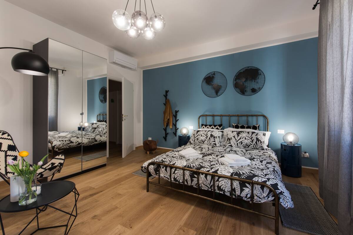 A modern bedroom with a large bed, a mirror, a desk, and a chair.