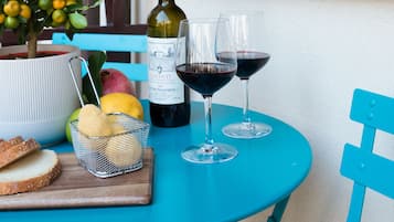Uma mesa com uma garrafa de vinho, duas taças, uma cesta de frutas e um vaso com planta.