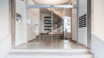 Entrada moderna de hotel com porta de vidro, escadaria para o andar superior e placa com a inscrição "Día La Mancomunidad".