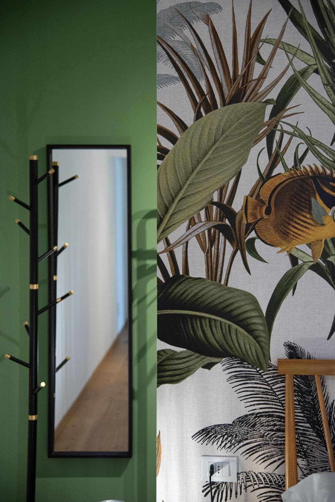 Una stanza con parete verde, uno specchio con cornice nera e un murale a tema tropicale con foglie grandi e un pesce.