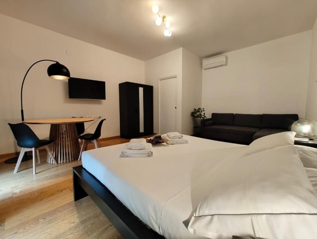 A modern hotel room with a bed, a desk, a chair, a sofa, and a TV mounted on the wall.