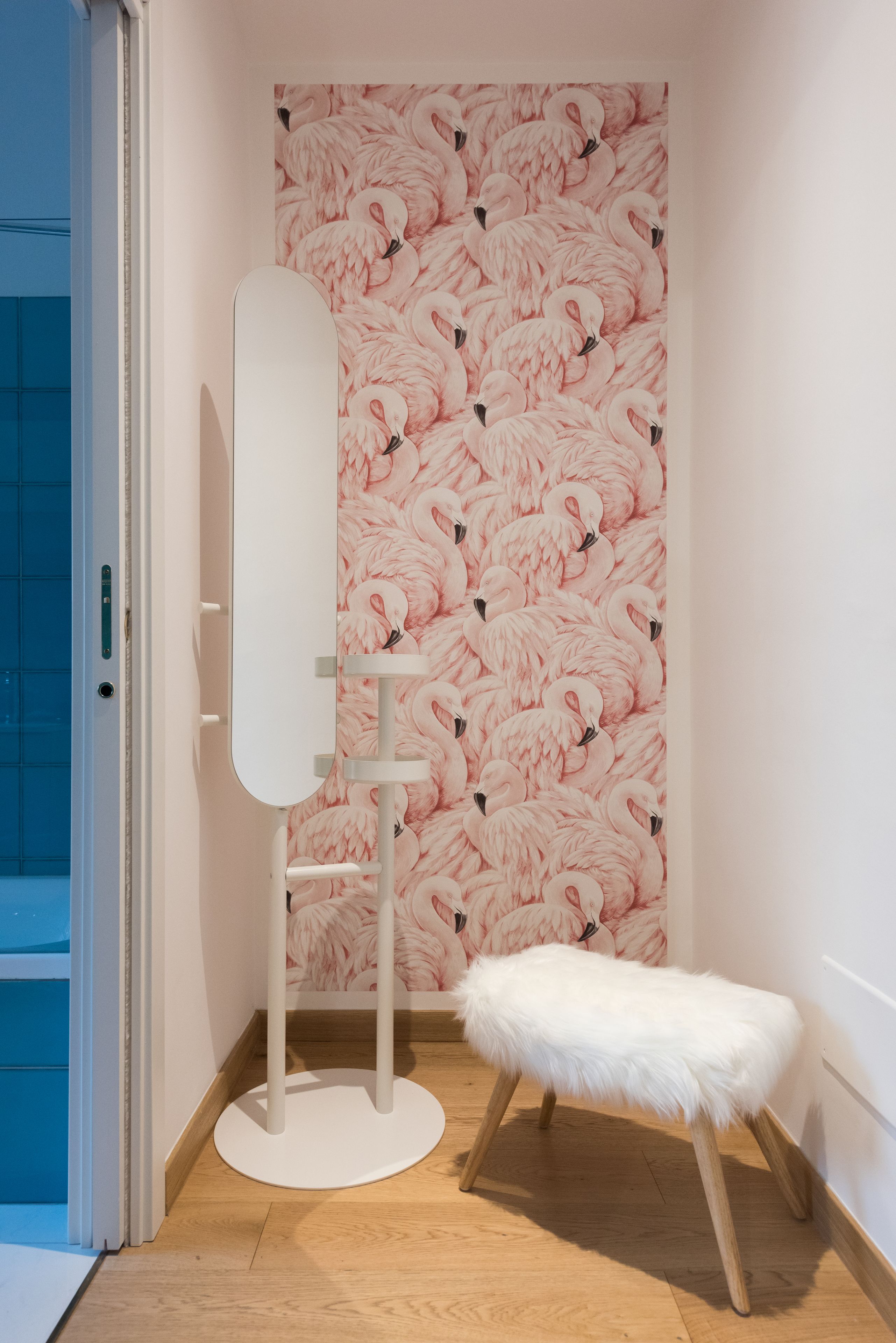 Um banheiro com papel de parede de flamingos rosa, um espelho com toucador branco e um banquinho branco fofo.