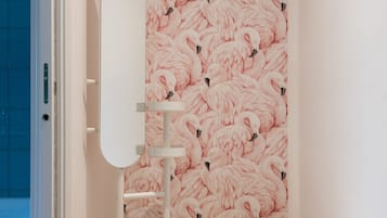 Um banheiro com papel de parede de flamingos rosa, um espelho com toucador branco e um banquinho branco fofo.